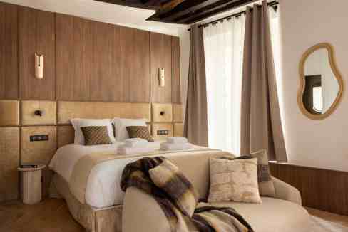 Elegant hotel bedroom with cozy seating area, neutral tones, and stylish decor.