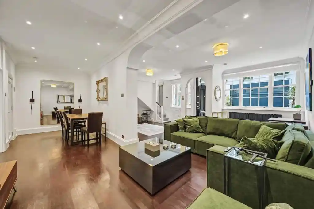 Spacious living room with green sofa and large windows in Sage Mews.