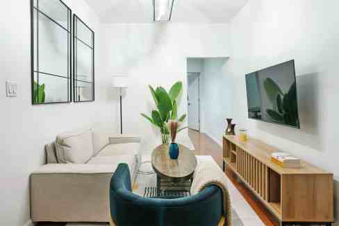 Contemporary living room featuring a beige sofa, blue armchair, and large wall-mounted TV with indoo.