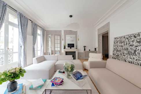 Bright and spacious living room with white sofas and large windows in Trocadéro Lumière House.