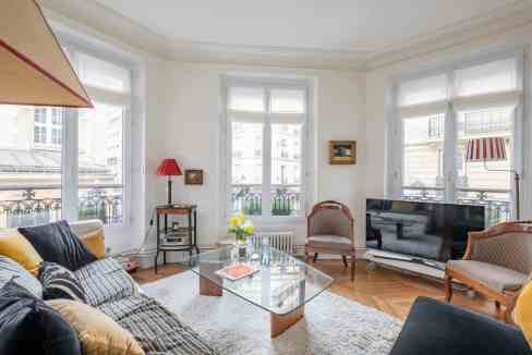 Spacious living room with large windows, elegant furniture, and natural light in Parisian style.