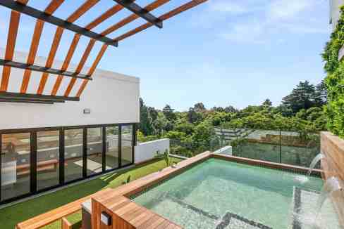 Rooftop pool with glass railing overlooking lush green landscape and modern architecture.