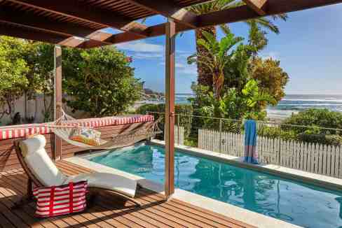 Poolside relaxation with ocean view, tropical plants, and shaded lounge area.