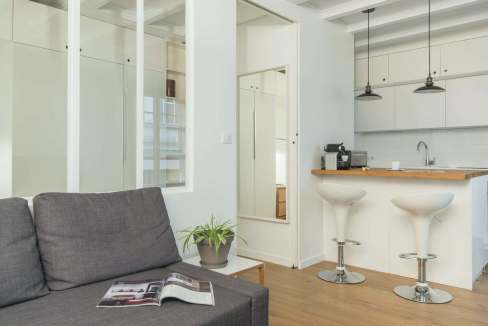 Bright modern living room with open kitchen, white cabinets, and bar stools.