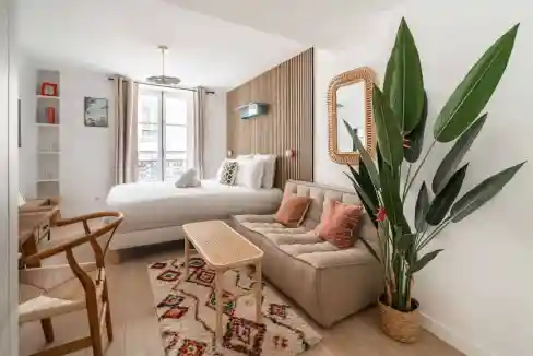 Bright and modern living space with a large bed, sofa, and green plant in a serviced apartment.