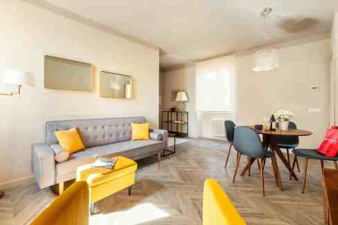 Stylish living room featuring a gray sofa with yellow cushions, a round dining table, and contempora.