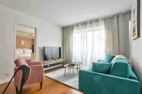 Modern living room with large window, teal sofa, pink armchair, and minimalist decor.