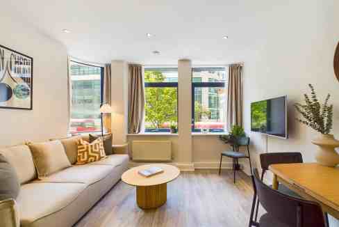 Bright living room with large windows, sofa, and TV in a serviced apartment.