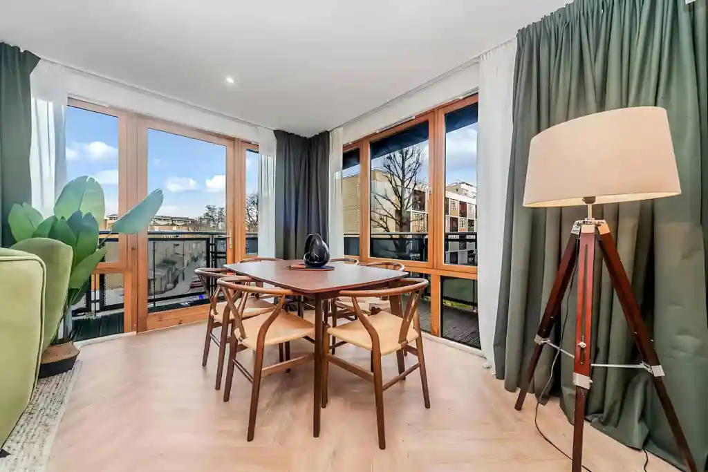 Bright living room with large windows, wooden dining table, and green curtains.