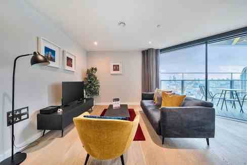 Contemporary living room with large window, sofa, armchair, and TV setup.