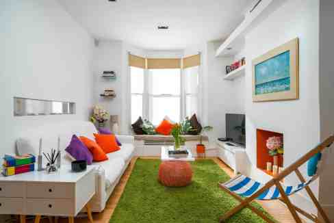 Coastal living room with white walls, colorful cushions, and large bay window.