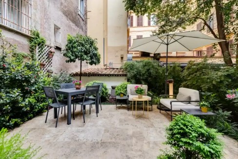 Outdoor garden with patio furniture, umbrella, and lush greenery in an urban setting.