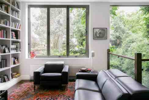Bright living room with large windows and black leather sofas.
