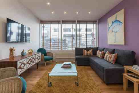Modern living room with large windows, purple accent wall, and stylish furniture.