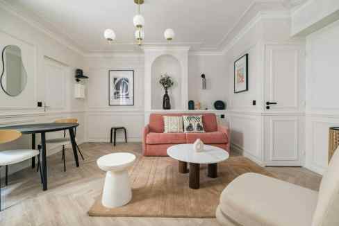 Modern minimalist living room with pink sofa, white walls, and stylish decor elements.