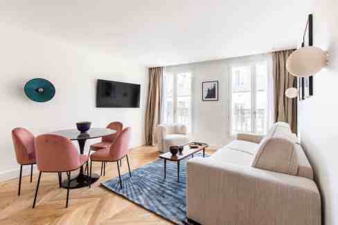 Bright living room with beige sofa, pink chairs, and large windows.