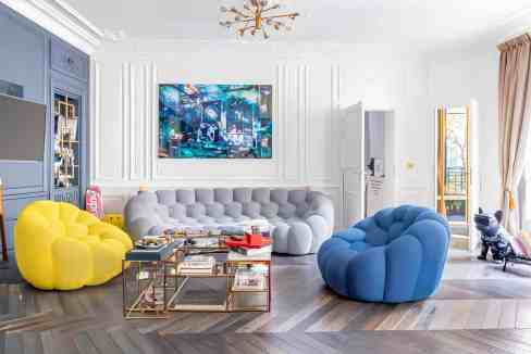Contemporary living room with colorful plush chairs and a large wall-mounted TV.