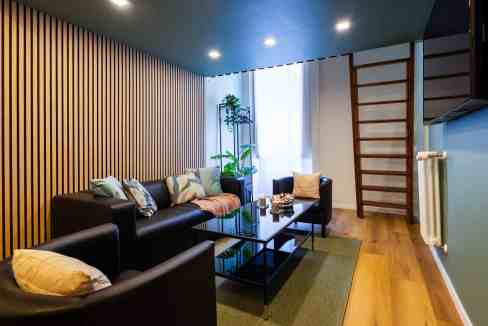 Elegant living room with black sofas, wooden wall, and natural light.
