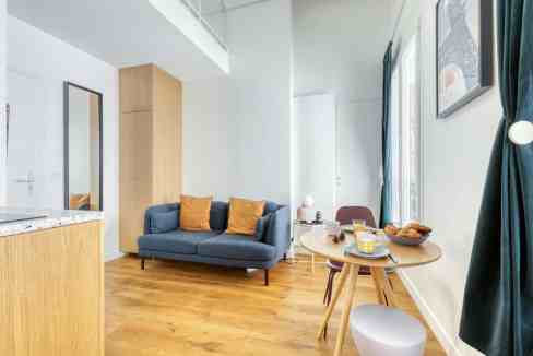 Cozy living room featuring a blue sofa with orange cushions and a small dining table with breakfast.