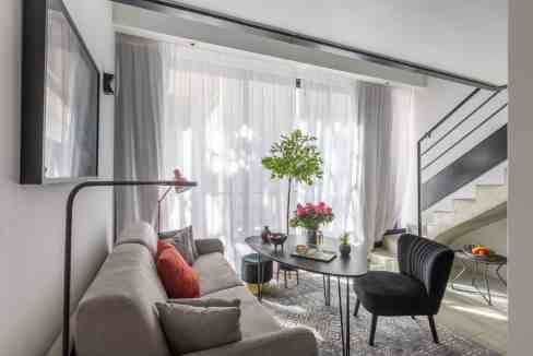 Bright living room with sofa, armchair, and large window with curtains.