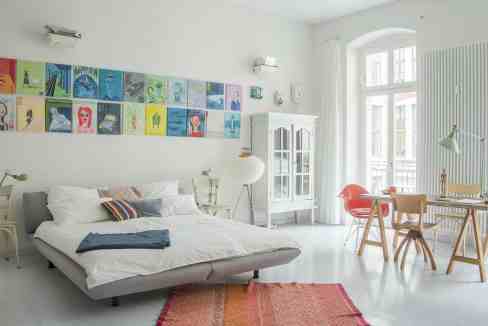 Bright minimalist bedroom featuring colorful art wall, white furniture, and large windows for natura.