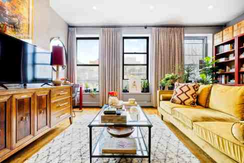 Bright living room with large windows, yellow sofa, and wooden furniture.