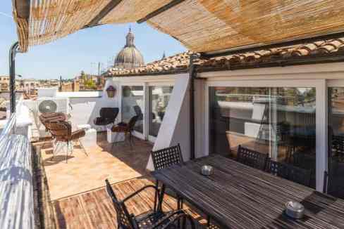Rooftop terrace with outdoor furniture, city skyline, and historic dome in the background.