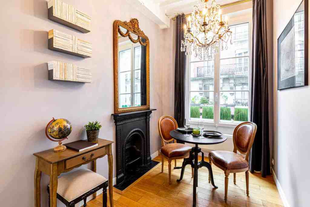 Elegant vintage dining corner with ornate mirror, chandelier, and classic furniture in a bright room.
