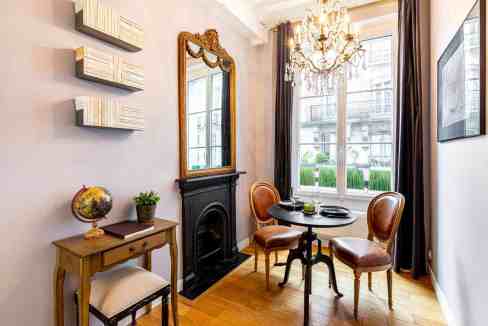Elegant vintage dining corner with ornate mirror, chandelier, and classic furniture in a bright room.