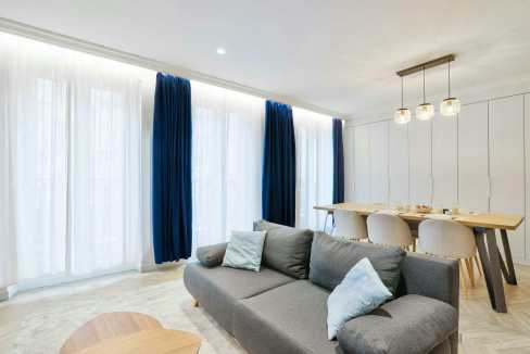 Bright living room with large windows, blue curtains, and contemporary furniture.
