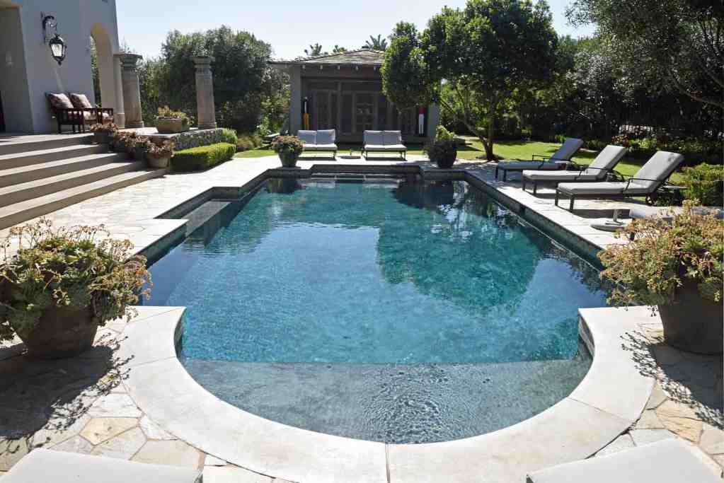 Elegant outdoor pool area with sun loungers, potted plants, and shaded seating.