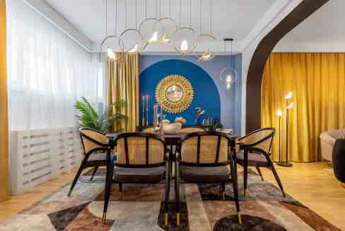 Modern dining room with colorful blue accent wall, elegant chandelier, and contemporary furniture.