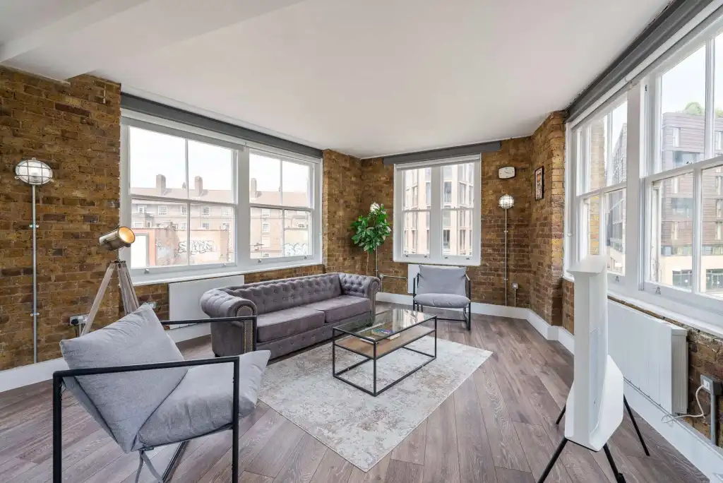 Bright, stylish living room in Shoreditch loft with exposed brick walls and large windows.