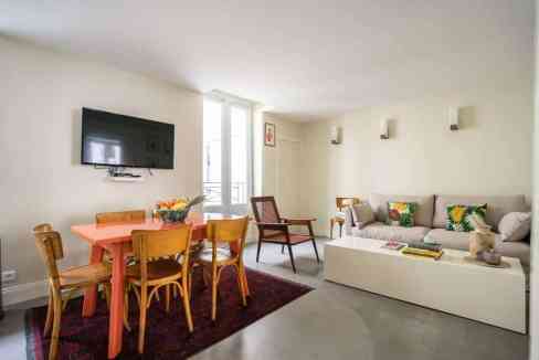Bright living room with sofa, dining table, and wall-mounted TV in Paris.
