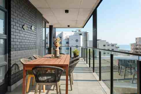 Outdoor balcony with dining table and chairs overlooking cityscape and ocean.