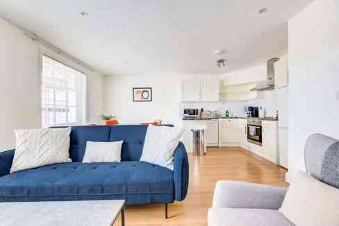 Bright living room in a serviced apartment with blue sofa and open kitchen.