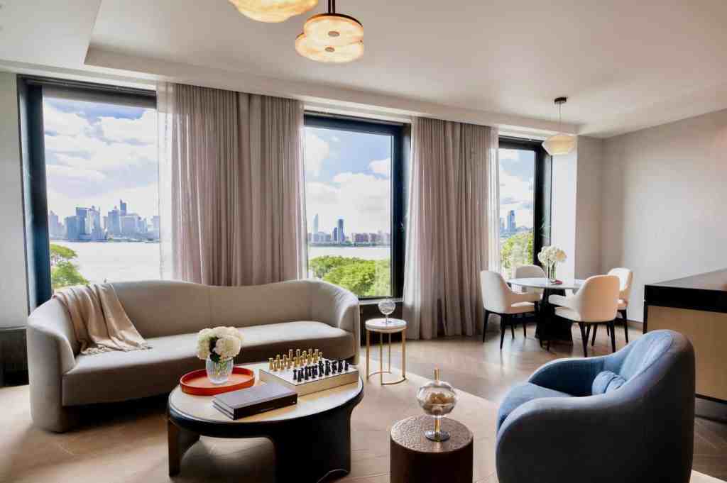 Bright living room with large windows overlooking the city skyline and river, featuring stylish furn.