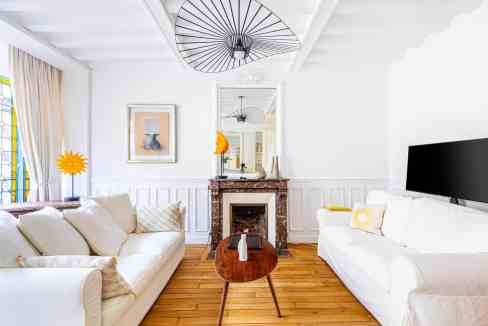Bright modern living room with white sofas, fireplace, and stylish decor elements.
