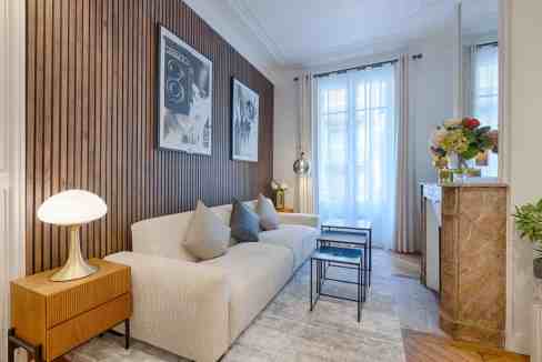 Bright living room with beige sofa, wooden wall, and large windows.