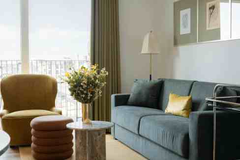 Modern living room with blue sofa, yellow pillow, and balcony view.