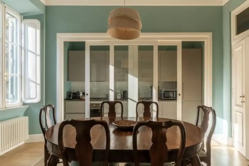 Elegant dining room with wooden table, chairs, and glass sliding doors in a bright, airy space.