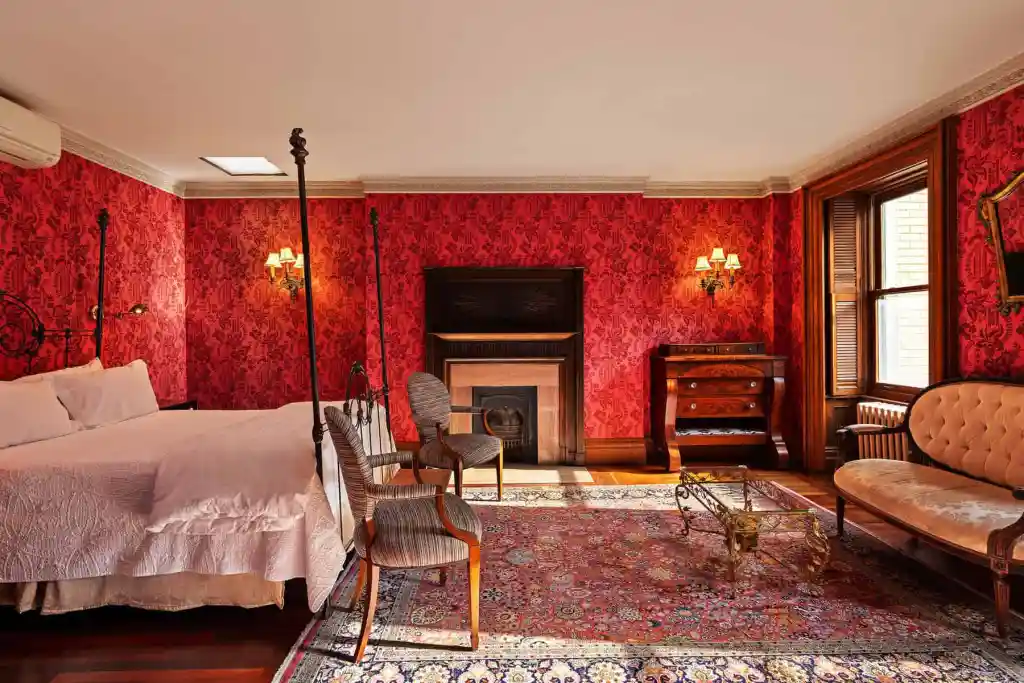 Victorian bedroom with red damask wallpaper, antique furniture, and cozy fireplace.