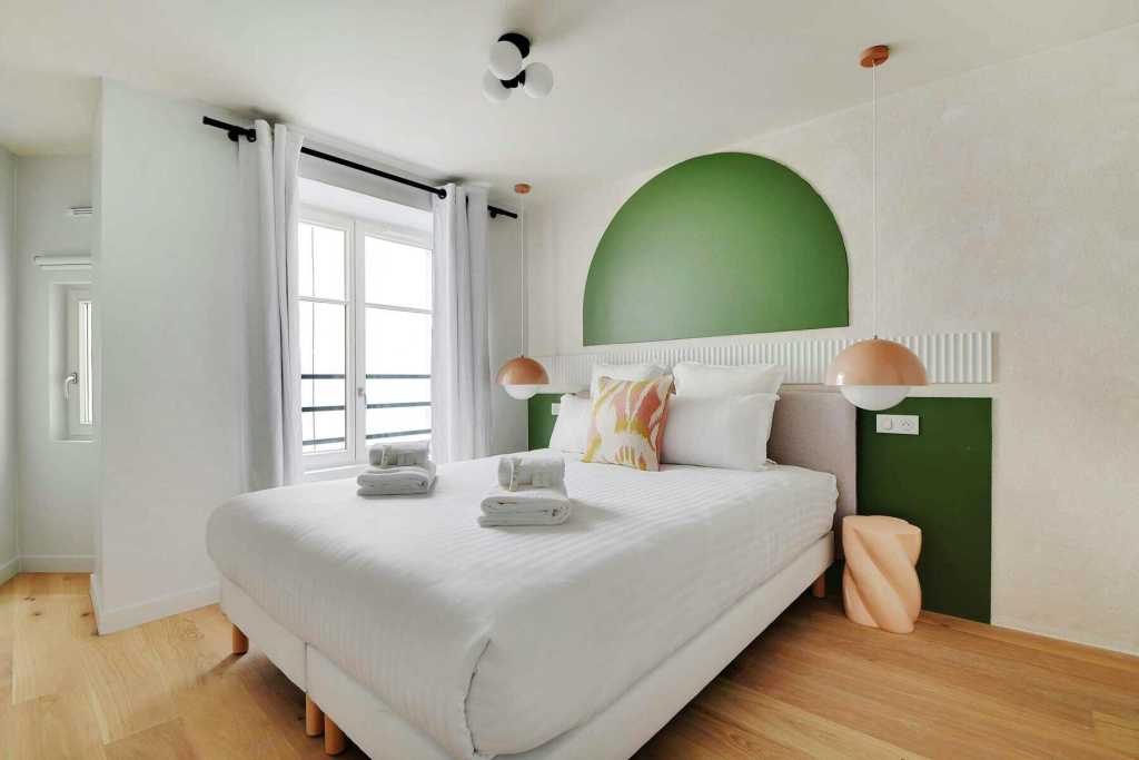 Bright bedroom with green accent wall, white bedding, and natural light.