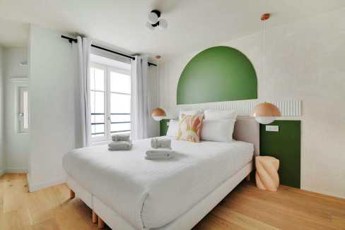 Bright bedroom with green accent wall, white bedding, and natural light.