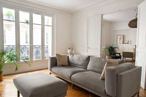 Bright living room with large windows, gray sofa, and stylish decor in Paris.