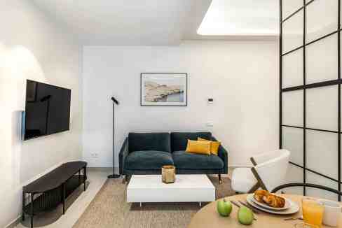 Contemporary living room featuring a dark green sofa, white armchair, and sleek black TV stand in a.