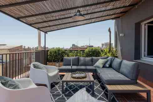 Rooftop balcony with outdoor sofa, chairs, and city skyline view.