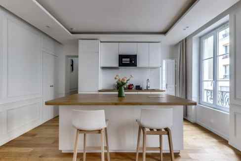 Elegant minimalist kitchen with white cabinets, wooden countertop, and ample natural light from larg.