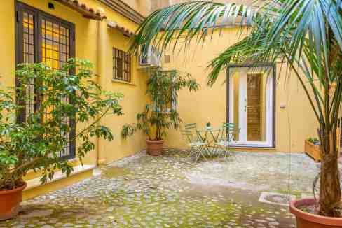 Bright yellow courtyard with lush green potted plants and outdoor seating area.