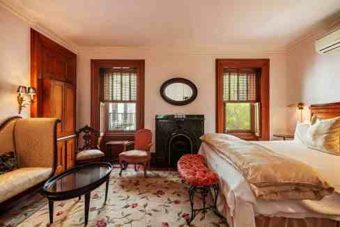 Cozy bedroom featuring vintage furniture, wooden accents, and natural light from large windows.